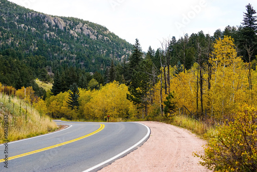 A winding road runs through Golden Gate Canyon State Park in Colorado with changing Aspen trees lining the road, and pine trees high up the mountainside.