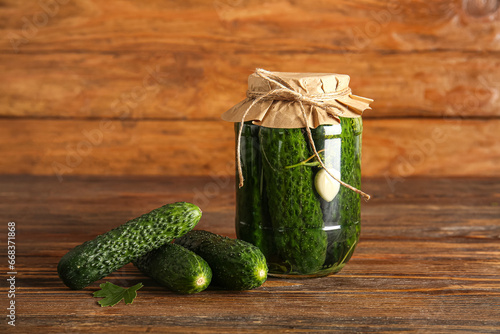 Jar with canned cucumbers and fresh vegetables on wooden background