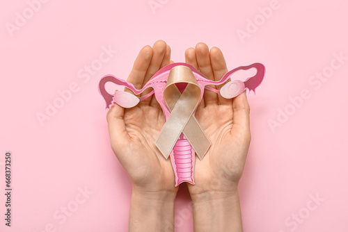 Woman with beige ribbon and paper uterus on pink background. Cancer awareness concept photo