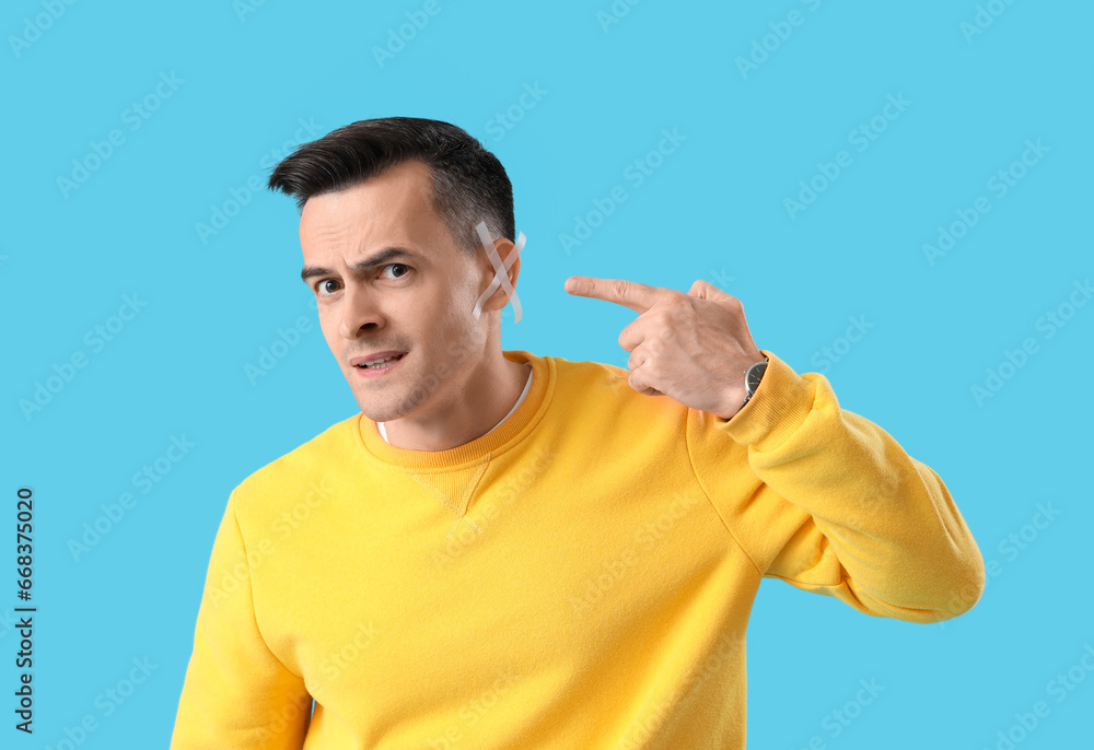 Young man with hearing problem on blue background Young man with hearing problem on blue background
