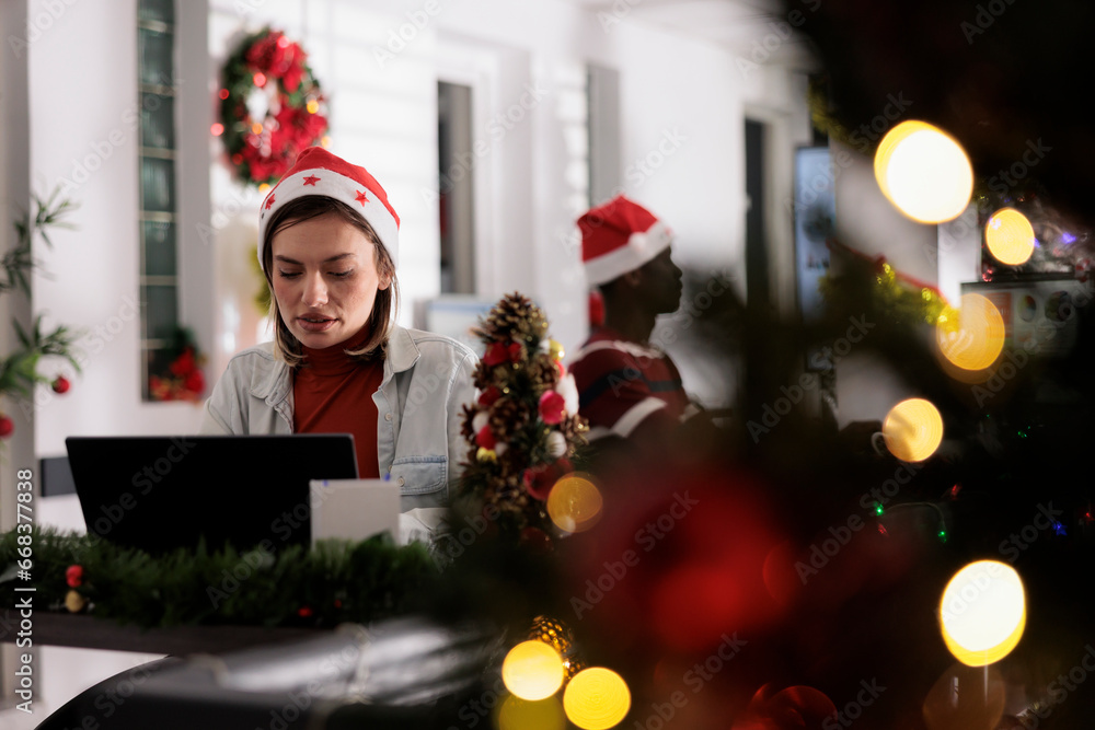 Businesswoman in festive decorated workspace working hard on computer tasks for upcoming project. Employee researches company startup plans during Christmas holiday season