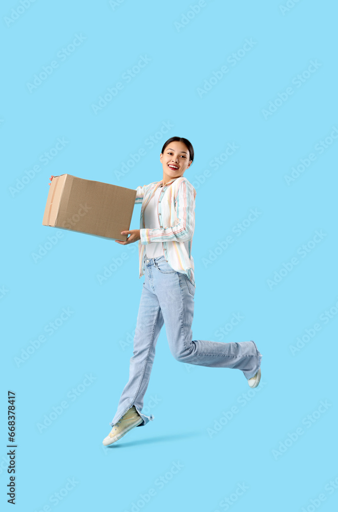 Young Asian woman with parcel jumping on blue background Young Asian woman with parcel jumping on blue background