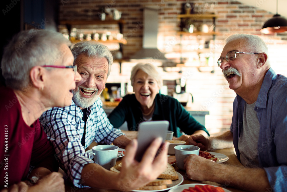 Four senior people using a smartphone and laughing Four senior people using a smartphone and laughing