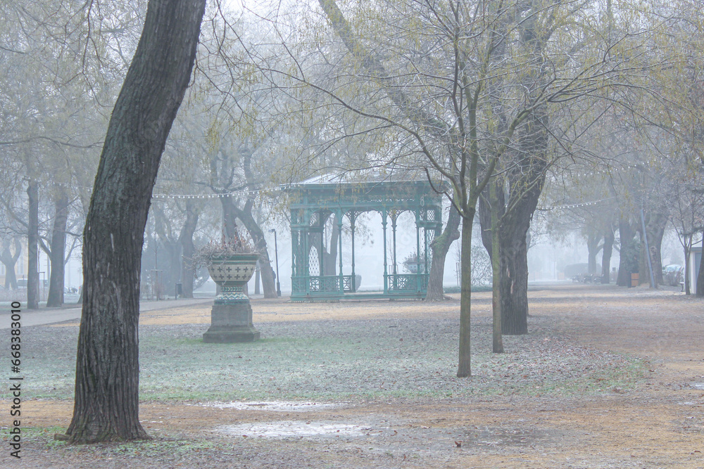Winter foggy park with an old green pavilion
