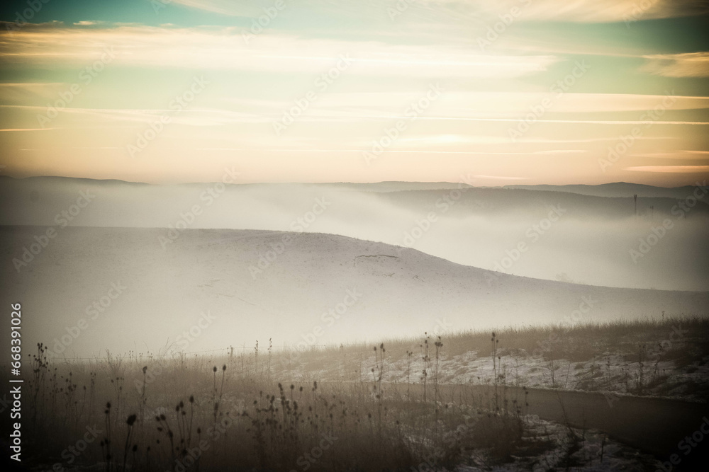 moody winter landscape with fog at sunset