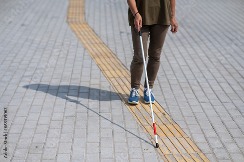 Close-up of the legs of an elderly blind woman with a cane at a tactile tile. photo