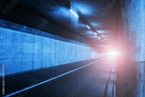 Horror tunnel background. Dark pavement tunnel with bright light at the end. Scary walkway under the bridge. Grunge urban bridge construction. Bright spot light at the end of a tunnel.