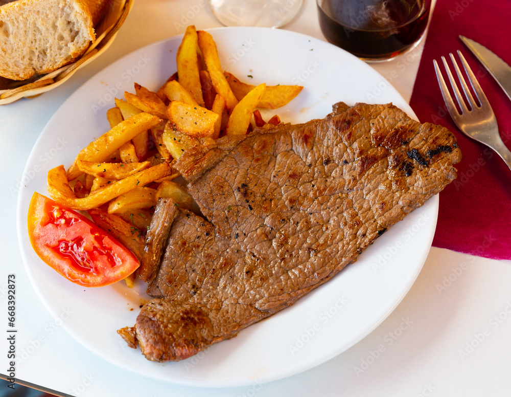 Fried juicy beef steak served with potatoes and tomatoes