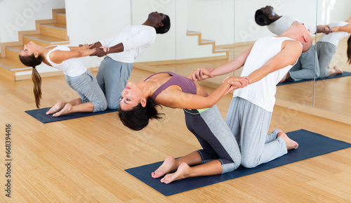 Two couples of young adult people practicing yoga lesson with partner at studio