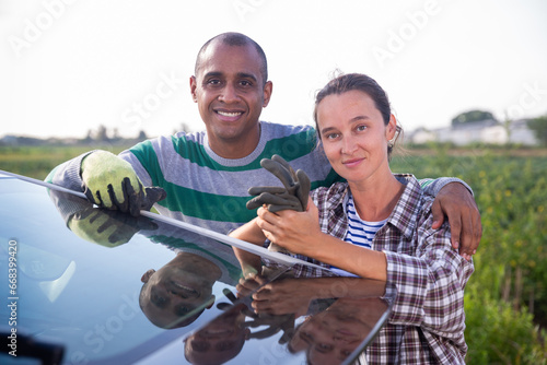 Smiling woman and man farm workers posing together standing near car outdoors © JackF