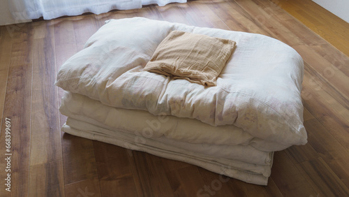 フローリングの上に畳んだ布団と枕 photo