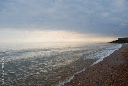 Wallpaper Mural Incoming Tide Atlantic Ocean Sea Ebbing and Flowing on Smooth Natural Stone Pebble Beach in England with Misty Stormy Horizon with Setting Sun Casting Pinks Oranges Peeking Through Stormfront  Torontodigital.ca