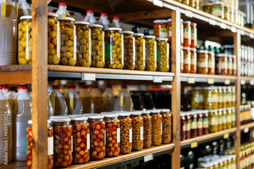 Marinated whole unpitted green olives in glass jars offered for sale on shelf rack in store. Traditional Spanish appetizer. Farm product. © JackF