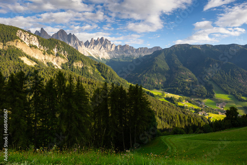 Picture of colorful nature, forest and meadows, against background of sky and mountains, in Val de Funes region, Dolomites. In distance are lonely rural houses of local residents © JackF
