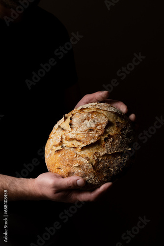 Attractive young Caucasian chef posing with white sourdough bread. The sourdough bread is the central protagonist of the scene, standing out with beautiful golden tones against the dark background.