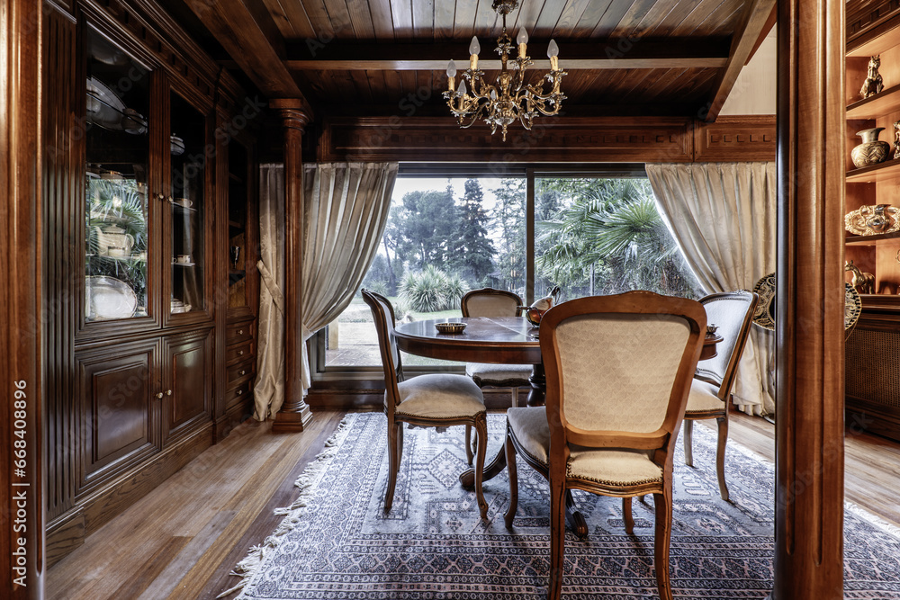 Living room of a classic house with matching mahogany wood furniture, circular table with upholstered chairs and a large window overlooking the garden Living room of a classic house with matching mahogany wood furniture, circular table with upholstered chairs and a large window overlooking the garden