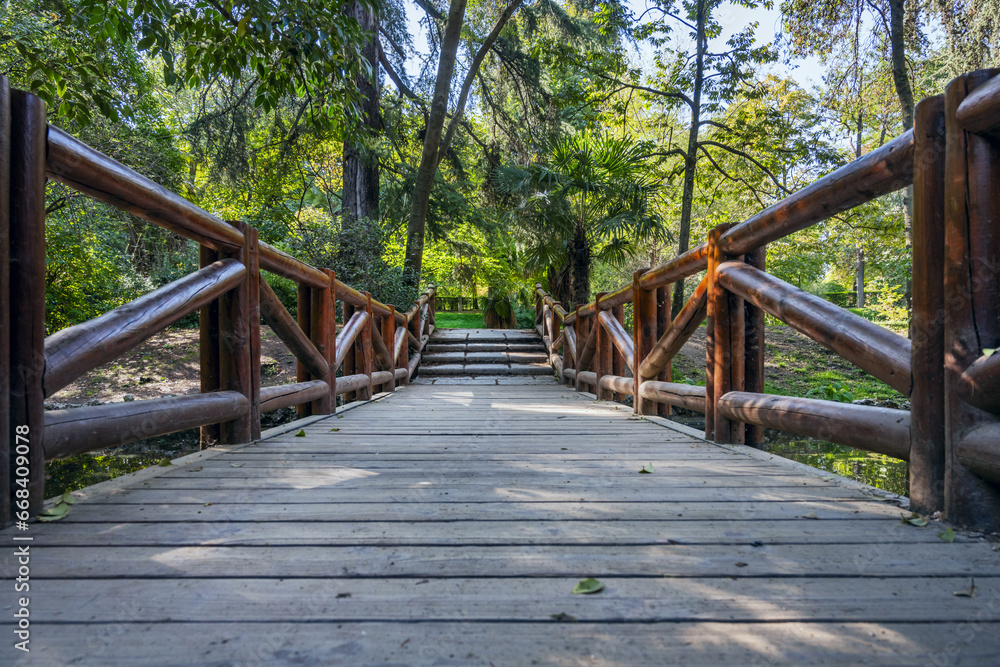 A rustic wooden bridge with log railings over a small stream in a heavily vegetated area within an urban park A rustic wooden bridge with log railings over a small stream in a heavily vegetated area within an urban park