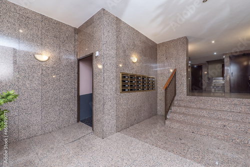Hallway of a residential apartment building with pink polished granite walls and floors, steps of the same material with metal railing and wooden handrails