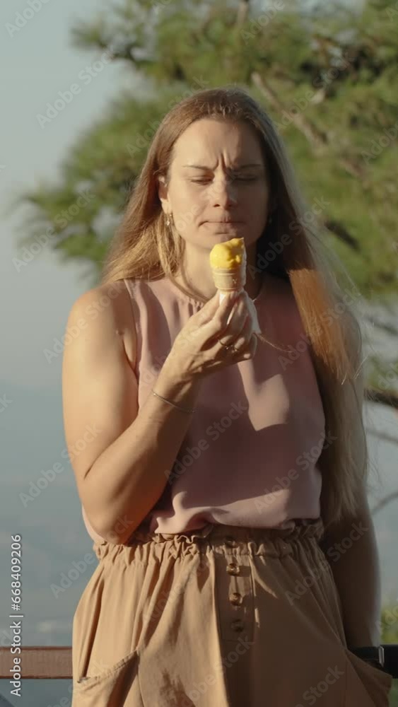 Vertical video. A young woman of European descent enjoys ice cream at sunset while standing at the top of a mountain in a tourist cafe. Vertical video. A young woman of European descent enjoys ice cream at sunset while standing at the top of a mountain in a tourist cafe.