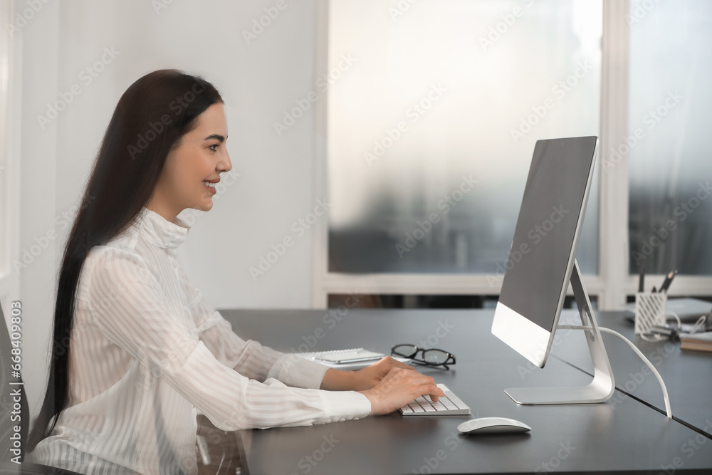 Happy woman using modern computer at black desk in office Happy woman using modern computer at black desk in office