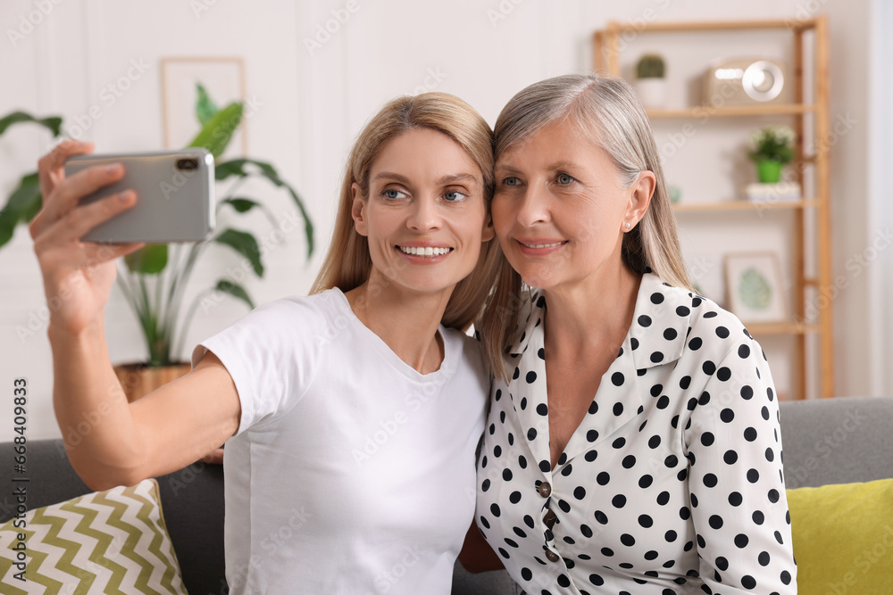 Happy daughter taking selfie with her mature mother at home