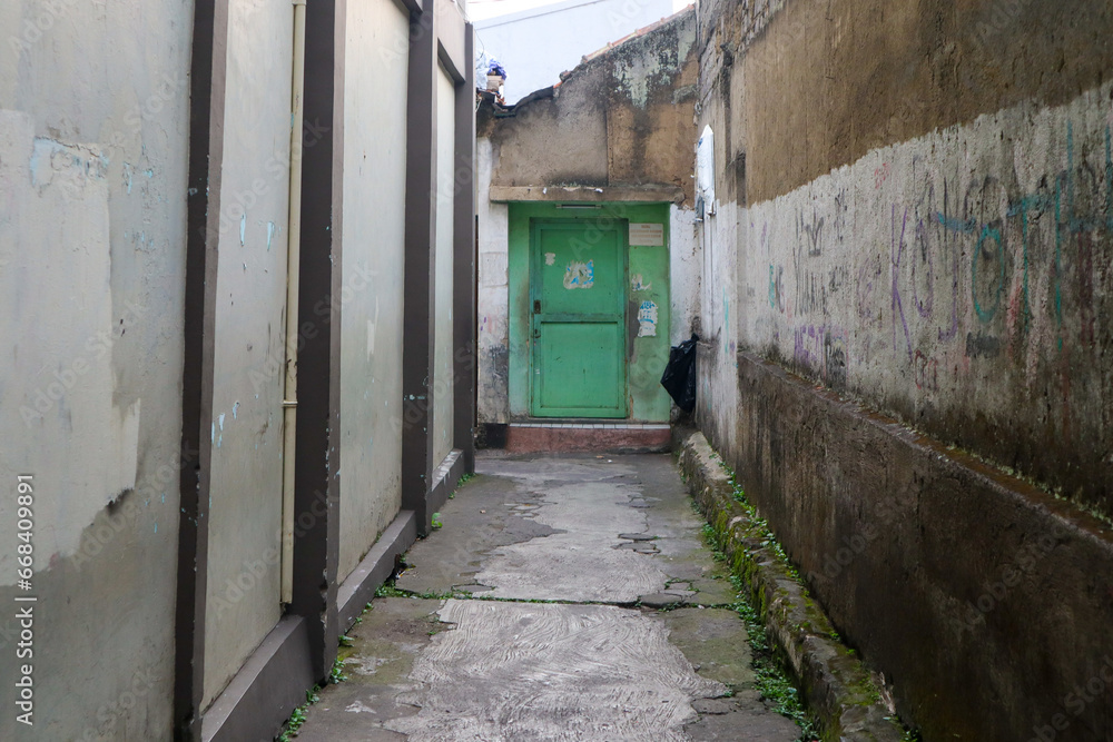 Cimahi, Indonesia - August 31, 2023. Green iron door at the end of the alley. Alleys with walls filled with vandalism.
