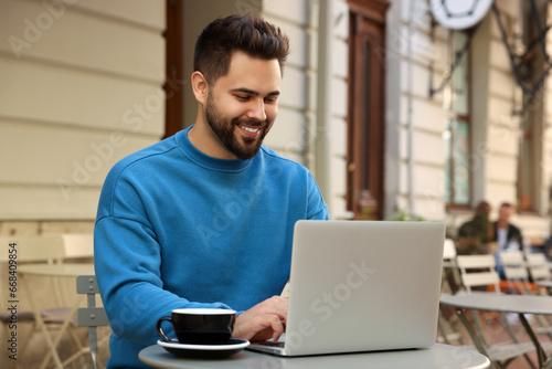Handsome young man working on laptop at table in outdoor cafe