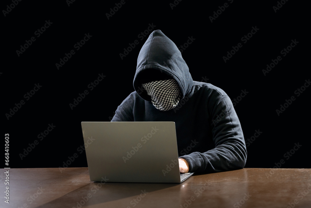 Hacker spy man one person in black hoodie sitting on table looking computer laptop used login password attack security to data digital in internet network system night dark background copy space Hacker spy man one person in black hoodie sitting on table looking computer laptop used login password attack security to data digital in internet network system night dark background copy space