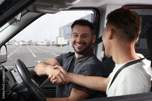 Driving school. Happy student shaking hands with driving instructor during lesson in car at parking lot