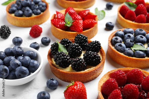 Tartlets with different fresh berries on white marble table. Delicious dessert