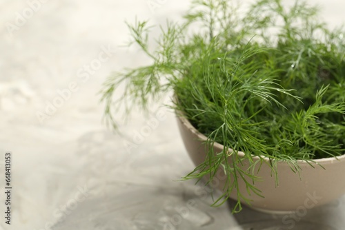 Bowl of fresh green dill on light grey table, closeup. Space for text
