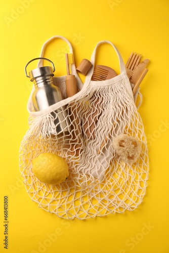 Fishnet bag with different items on yellow background, top view. Conscious consumption