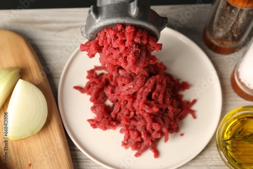 Mincing beef with metal meat grinder on light wooden table, closeup