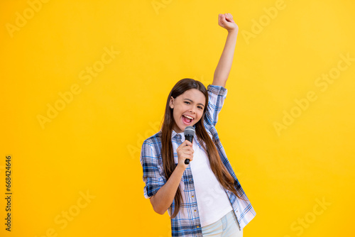 glad teen girl singer hold mic in studio perform karaoke isolated on yellow background