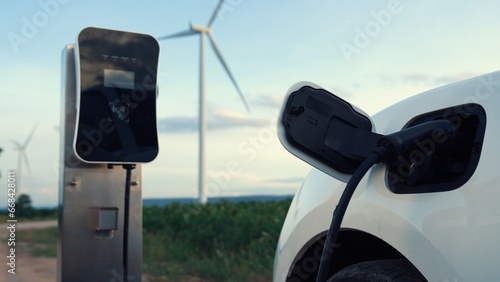 Progressive future energy infrastructure concept of electric vehicle being charged at charging station powered by green and renewable energy from a wind turbine in order to preserve the environment.