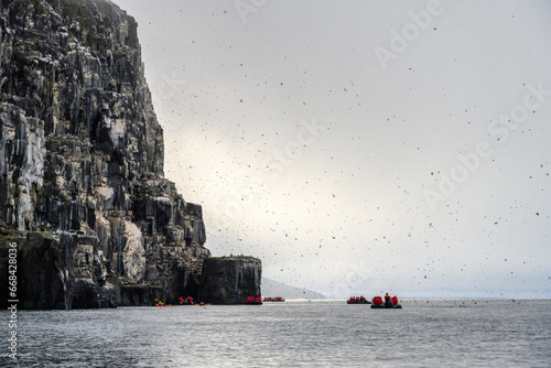 Small boats of tourists watching Brunnich's Guillemots nesting on bird cliffs on Mount Guillemot on Nordauslandet in the Hinlopen Straight, arctic tourism expedition around Svalbard 