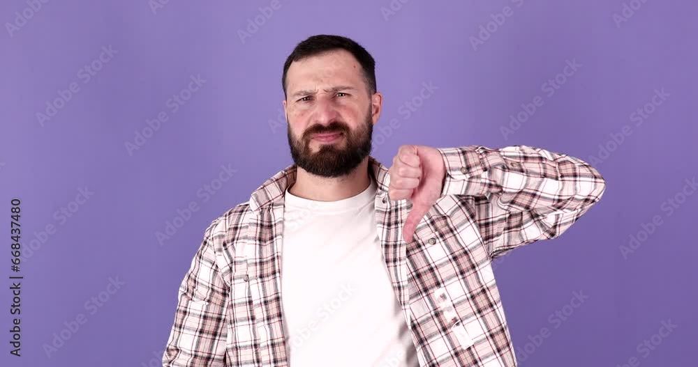Young bearded man doing negative gesture with thumbs down over isolated purple background. Young bearded man doing negative gesture with thumbs down over isolated purple background.