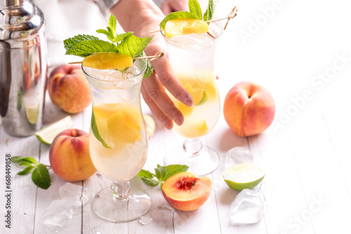 A hand reaching to take a peach mojito cocktail, against a bright background.