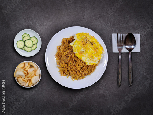 A plate of magelangan (burjo style), served with fried egg, kerupuk or chips, and cucumbers, on a dark background. Magelangan is Indonesian fried rice with noodles, popular in Central Java. photo