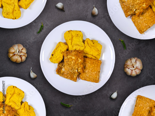 Fried tempe and tofu on white plates with garlics scattered around the plate. Indonesian recipe for tempe and tahu goreng. photo