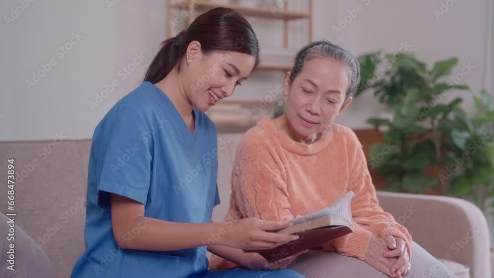 An Asian female caregiver reads a novel to an elderly Asian woman seated on a living room sofa. This image reflects the dedicated care and companionship offered to seniors at home. An Asian female caregiver reads a novel to an elderly Asian woman seated on a living room sofa. This image reflects the dedicated care and companionship offered to seniors at home.