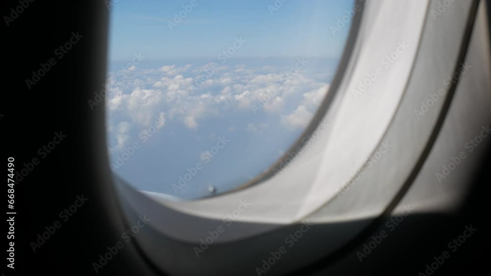 Aerial view through plane window with view over puffy white cloud with clear blue sky while flying, View from the window of the plane traveling by air Aerial view through plane window with view over puffy white cloud with clear blue sky while flying, View from the window of the plane traveling by air
