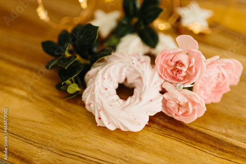 Pink merengue cookies and pink roses on a wooden brown natural table against a background of bokeh of New Year’s golden lights. Engagement ring with diamonds. Christmas background. Valentine’s Day © Liudmila