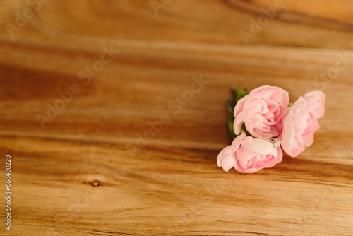 Delicate pink roses and an engagement ring with diamond on a wooden background close-up. Pink carnations. Place for text. Mock up. Gift for Mother’s Day, International woman’s day, Valentine’s Day.