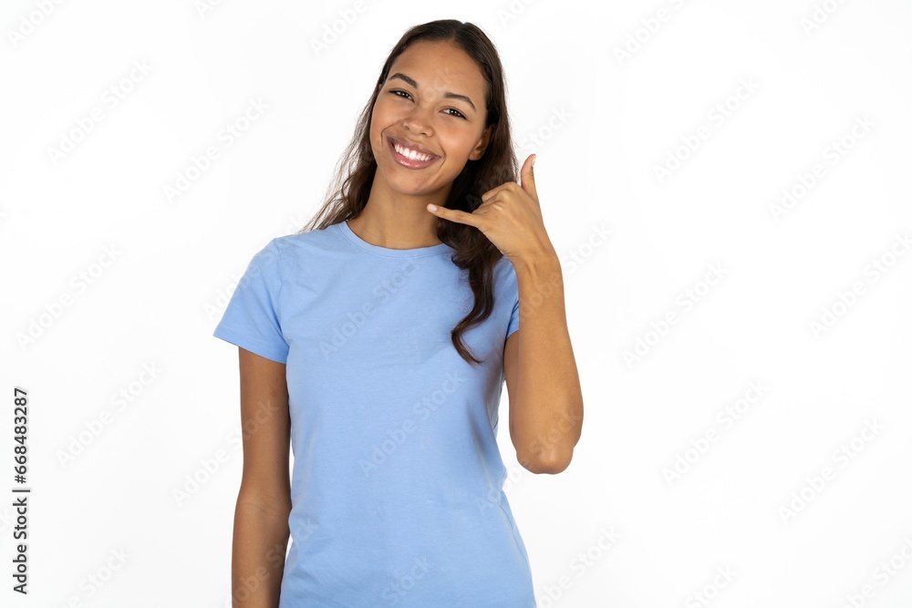 Beautiful girl wearing blue T-shirt smiling doing phone gesture with hand and fingers like talking on the telephone. Communicating concepts. Beautiful girl wearing blue T-shirt smiling doing phone gesture with hand and fingers like talking on the telephone. Communicating concepts.
