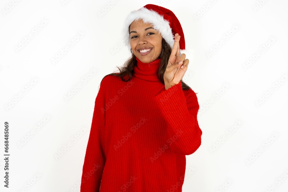 Beautiful girl wearing red sweater and Santa hat pointing up with fingers number ten in Chinese sign language Shi Beautiful girl wearing red sweater and Santa hat pointing up with fingers number ten in Chinese sign language Shi