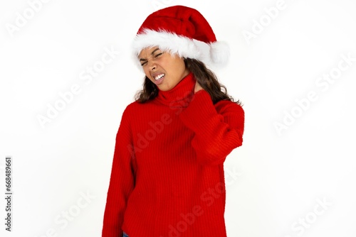 Beautiful woman wearing christmas hat Suffering of neck ache injury, touching neck with hand, muscular pain