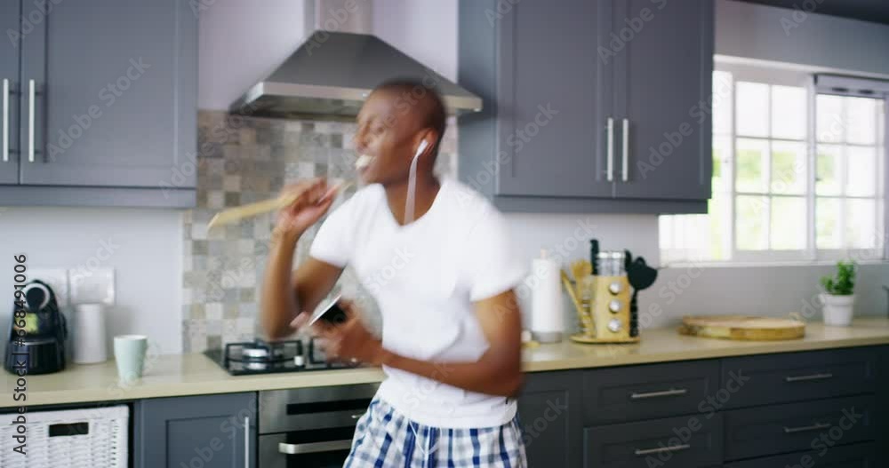 Happy man, singing and dancing with earphones in kitchen with spatula for mic. African person, phone and mobile app for performance, freedom and wellness with movement, fun and excitement in home Happy man, singing and dancing with earphones in kitchen with spatula for mic. African person, phone and mobile app for performance, freedom and wellness with movement, fun and excitement in home