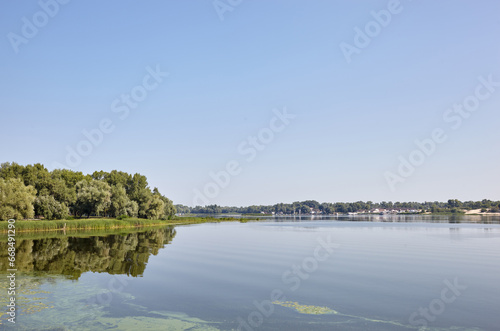 Scenery with dense trees near the river in Kyiv, Europe. Pier with parked yachts on background