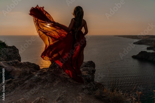 Woman sunset sea red dress, side view a happy beautiful sensual woman in a red long dress posing on a rock high above the sea on sunset.